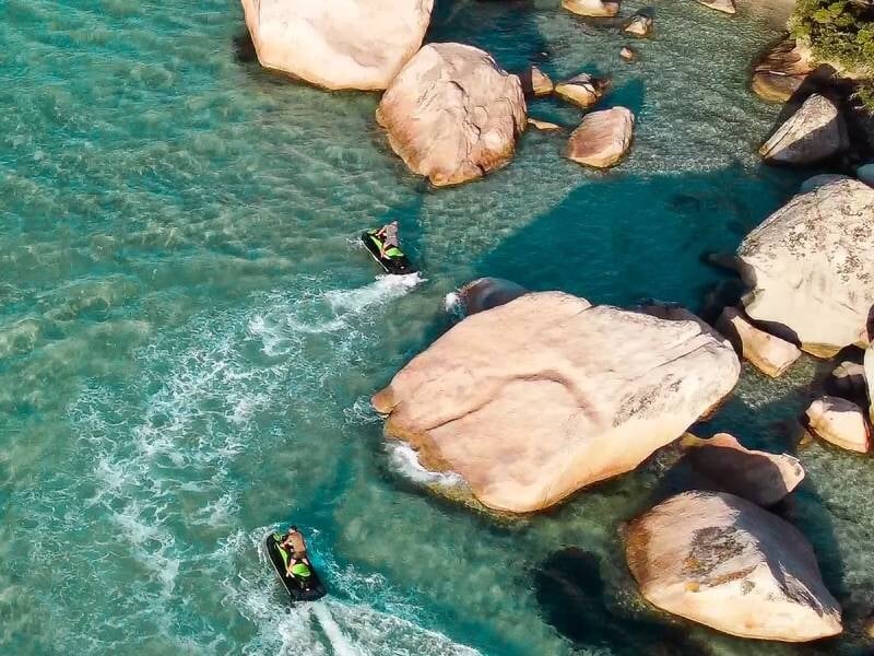Deux jetskis se faufilant entre de gros rochers dans une eau transparente aux nuances de bleu et vert, lors d'une randonnée au départ de Santa-Giulia.