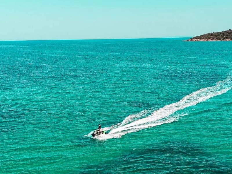 Jetski solitaire glissant sur une mer calme et turquoise avec une petite île visible à l'horizon.