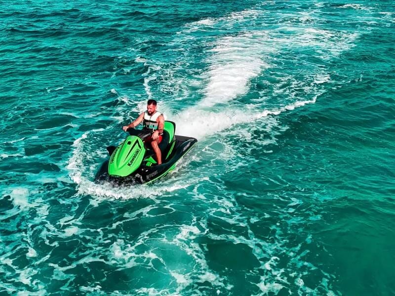 Homme conduisant un jetski vert sur une mer turquoise avec des vagues blanches autour de l'appareil.