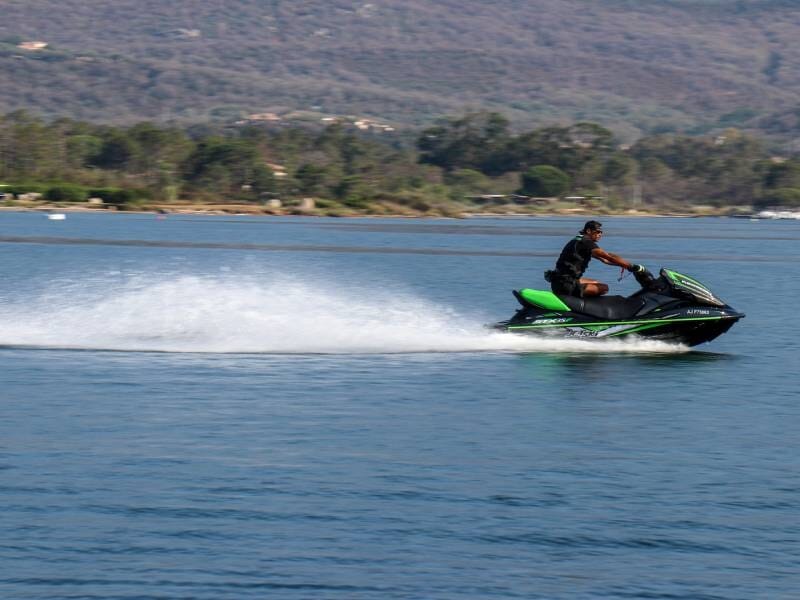 Personne sur un jetski vert et noir glissant rapidement sur une eau calme avec des montagnes en arrière-plan.