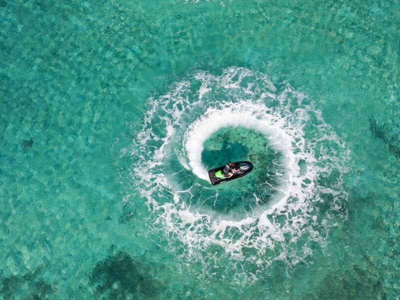 Vue aérienne d'un jetski noir et vert effectuant un cercle parfait sur une eau claire et peu profonde, lors d'une randonnée au départ de Porto-Vecchio.