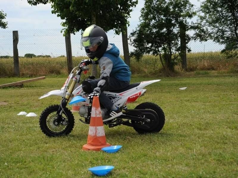 Enfant en casque conduisant une petite moto tout-terrain sur une pelouse avec des cônes d'entraînement.