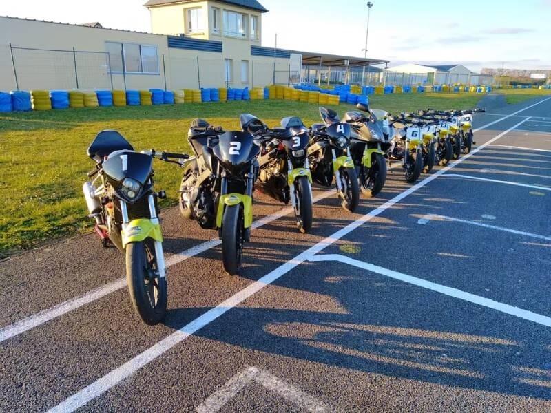 Alignement de plusieurs motos de course noires et jaunes stationnées sur une piste de circuit au soleil.