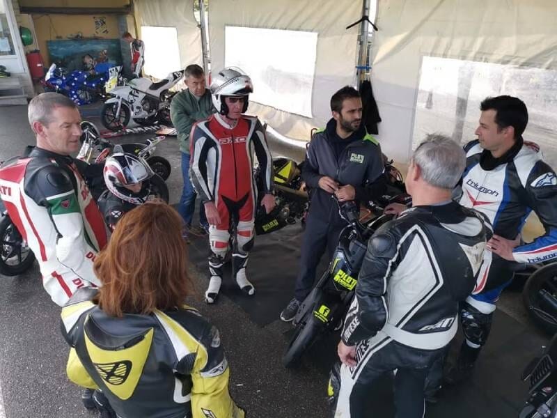 Groupe de motards en combinaison discutant dans un abri avec leurs motos visibles en arrière-plan.
