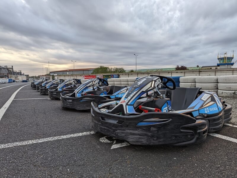 Rangée de karts bleus et noirs stationnés sur la piste du circuit de karting d'Albi sous un ciel nuageux.