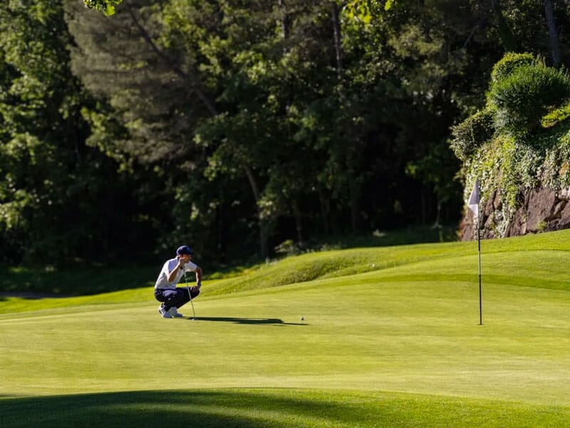 Golfeur accroupi sur un green, concentré pour aligner son coup près du drapeau sur un terrain bien entretenu.