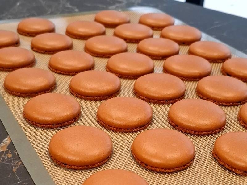 Plusieurs coques de macarons au chocolat posées sur un tapis de cuisson en silicone, prêtes à être garnies.