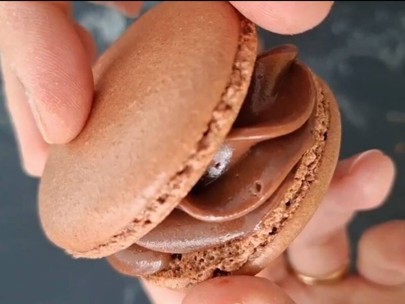 Gros plan sur un macaron au chocolat tenu à la main, montrant la ganache onctueuse à l'intérieur, lors d'un atelier pâtisserie à Reims.