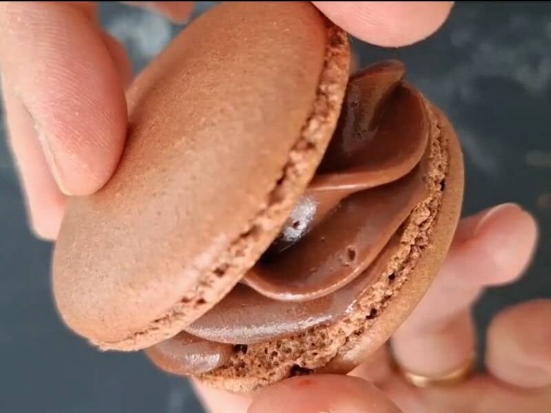 Gros plan sur un macaron au chocolat tenu à la main, montrant la ganache onctueuse à l'intérieur, lors d'un atelier pâtisserie à Reims.