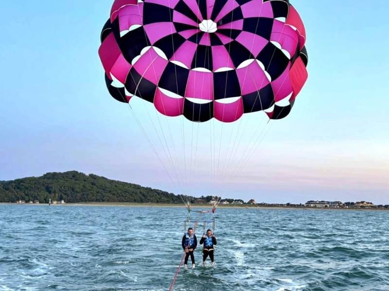 Deux personnes en parachute ascensionnel au-dessus de la mer, tirées par un bateau près de la côte verte.
