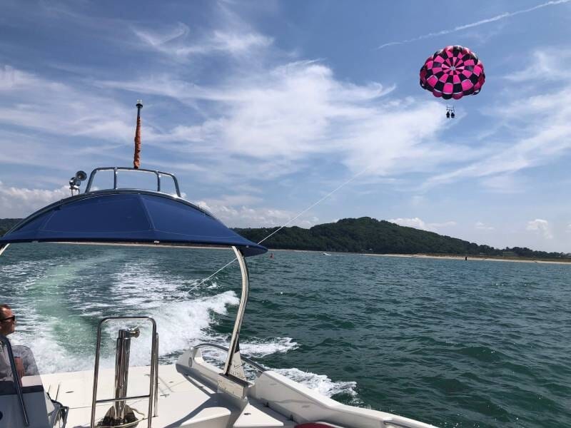 Vue depuis un bateau en mer avec un parachute ascensionnel rose et noir dans le ciel, paysage côtier en arrière-plan, lors d'un vol près de Cabourg.