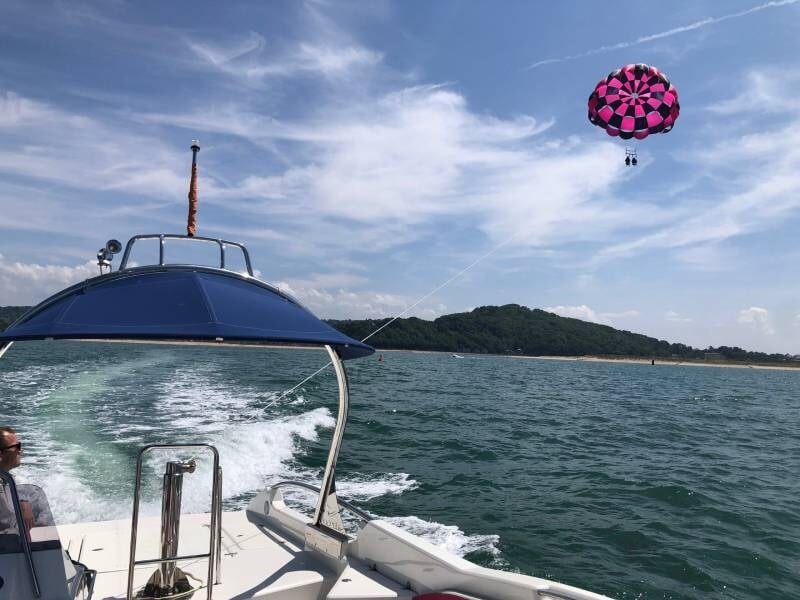 Vue depuis un bateau en mer avec un parachute ascensionnel rose et noir dans le ciel, paysage côtier en arrière-plan, lors d'un vol près de Cabourg.