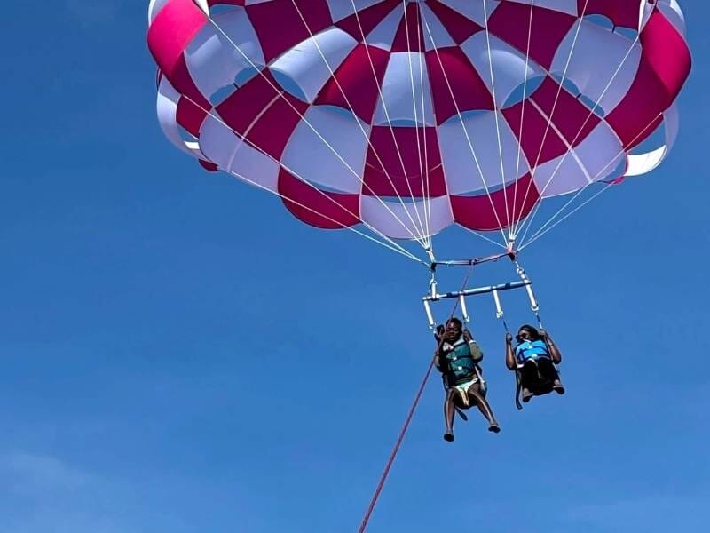 Deux personnes en parachute ascensionnel suspendues dans le ciel bleu, attachées à un bateau hors champ.