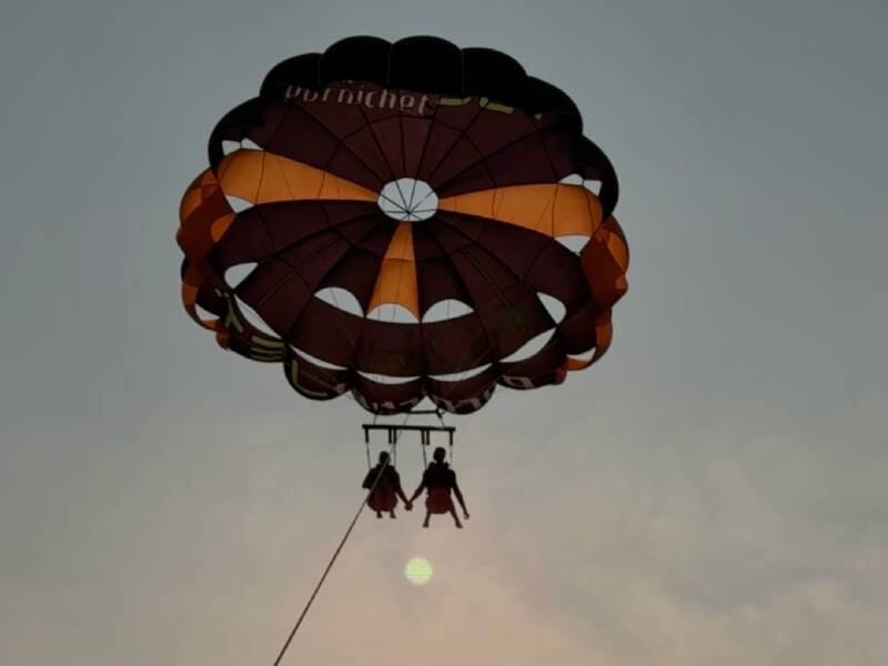 Deux personnes en parachute ascensionnel sous un parachute marron et orange au coucher du soleil.