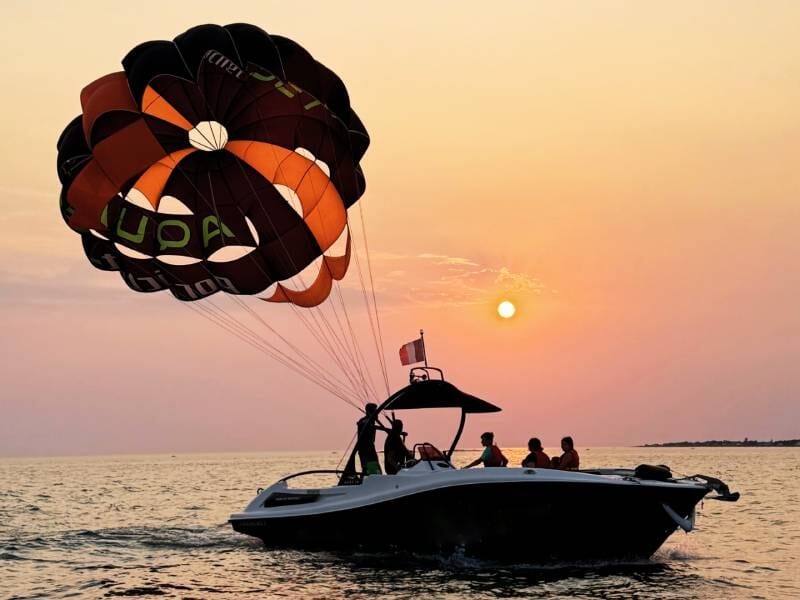 Bateau avec plusieurs personnes préparant un parachute ascensionnel au coucher du soleil sur la mer près de La Baule.