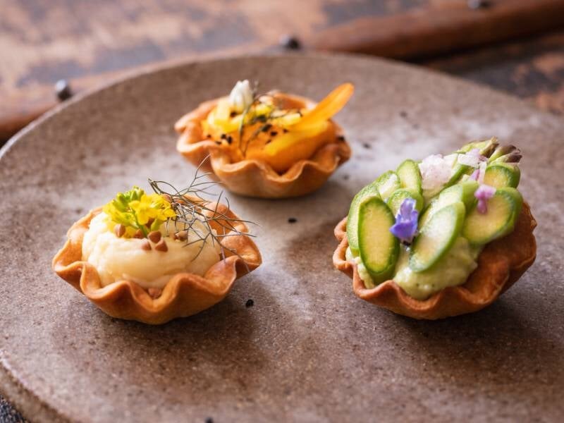 Trois mini tartelettes salées garnies de légumes frais et herbes, présentées sur une assiette en céramique rustique.