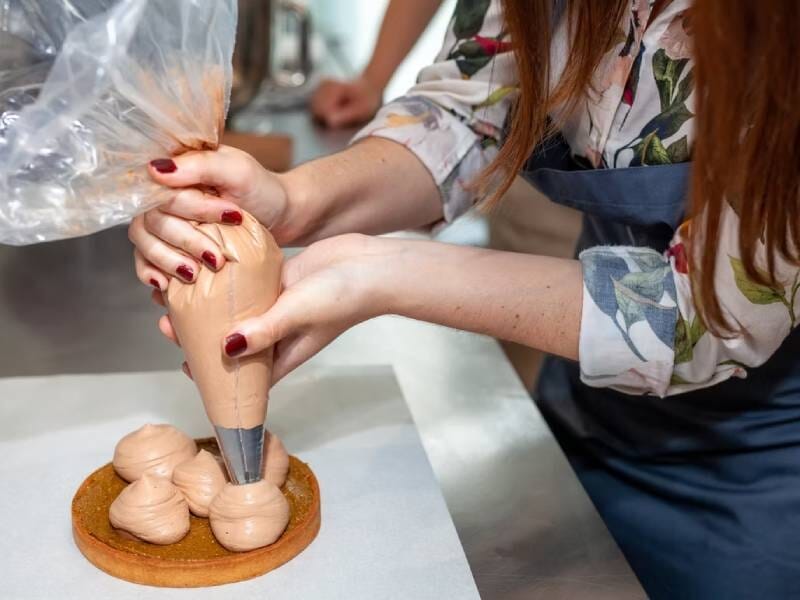 Une personne utilise une poche à douille pour décorer une pâtisserie sur un plan de travail en cuisine.