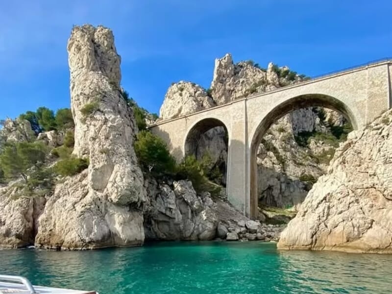 Vue d'un pont en arc surplombant des rochers blancs lors d'une balade en bateau à Marseille. 