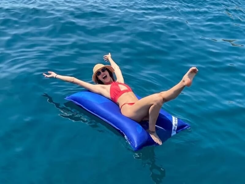 Femme en maillot rouge allongée et souriante sur un matelas lors d'une balade en bateau à Marseille.