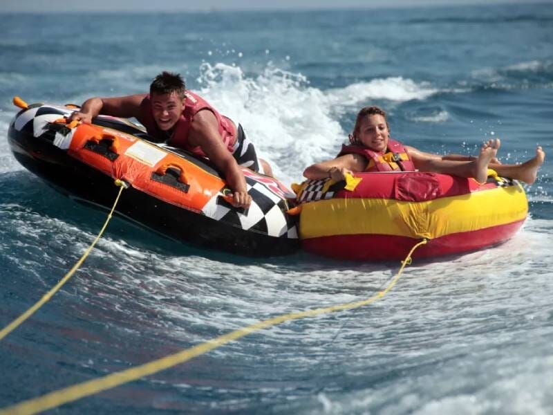 Deux jeunes s'amusent sur des bouées tractées sur une mer agitée, souriants et portant des gilets de sauvetage, à Six-Fours-les-Plages.