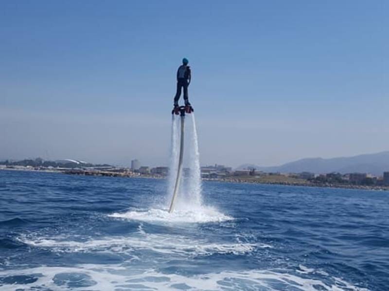 Personne en flyboard s'élevant au-dessus de la mer avec un ciel clair et une côte en arrière-plan.