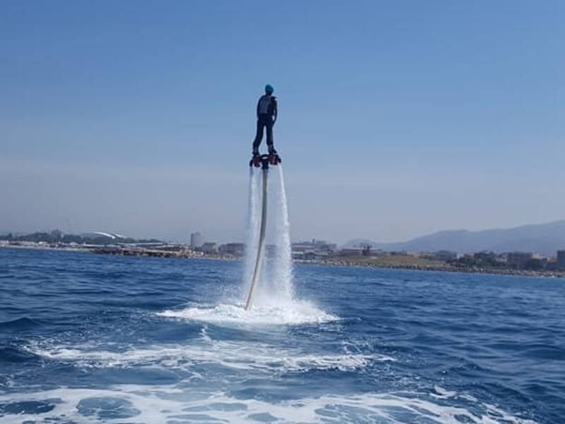 Personne en flyboard s'élevant au-dessus de la mer avec un ciel clair et une côte en arrière-plan.