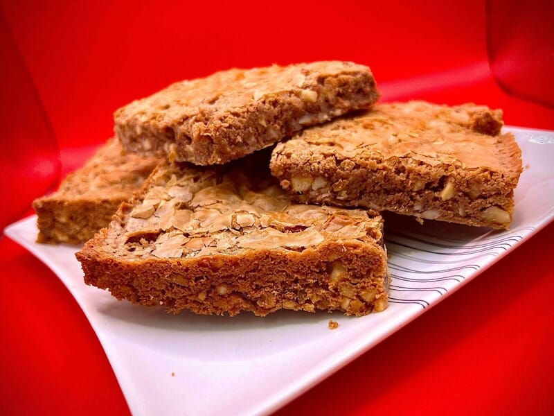 Carrés de gâteau croustillants aux noix présentés sur une assiette blanche avec un fond rouge vif.