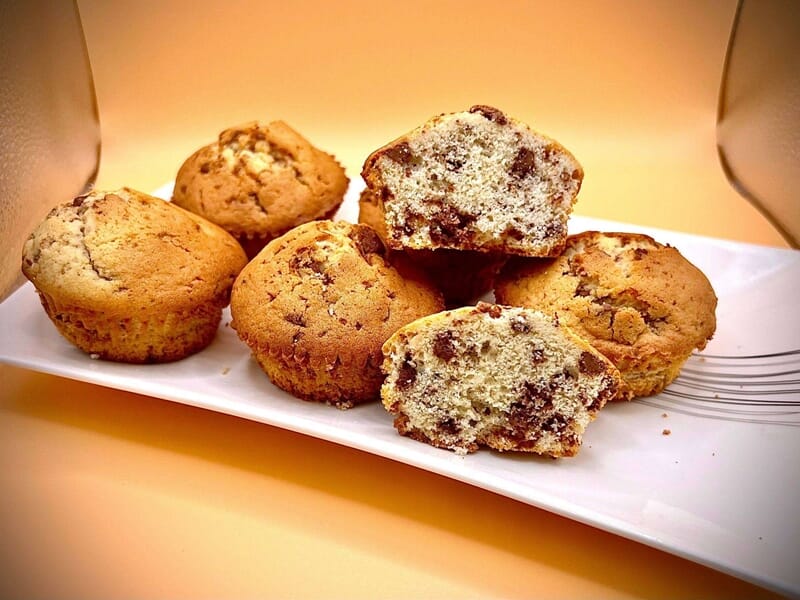 Muffins moelleux aux pépites de chocolat, certains coupés en deux, sur une assiette blanche.