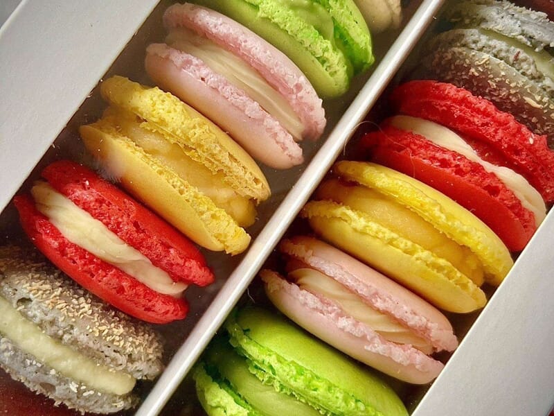 Boîte ouverte contenant des macarons colorés variés, avec une garniture crémeuse visible.