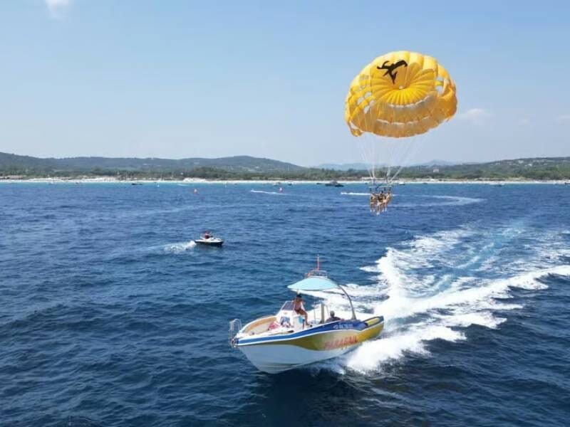Parachute ascensionnel au-dessus de la mer, tracté par un bateau rapide sur l'eau bleue à Pampelonne.