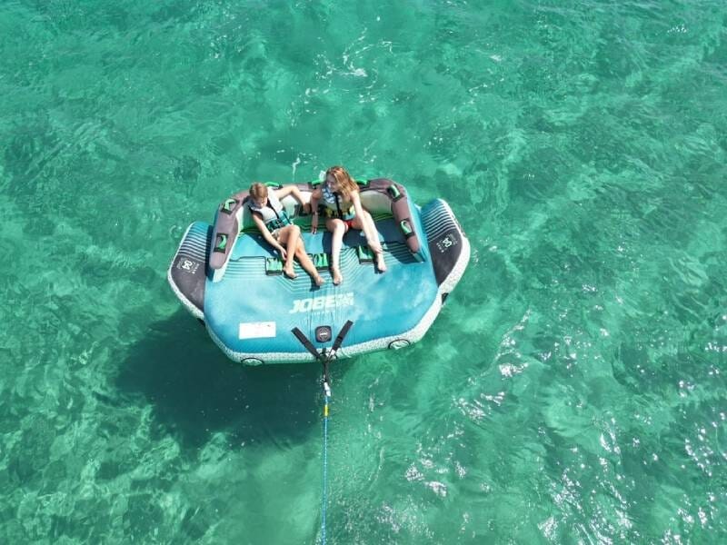 Deux personnes assises sur une grande bouée tractée bleue sur une mer turquoise, vues de dessus.