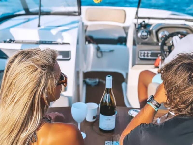 Deux personnes assises sur un bateau, profitant d'une bouteille de vin et de la mer bleue autour d'eux.