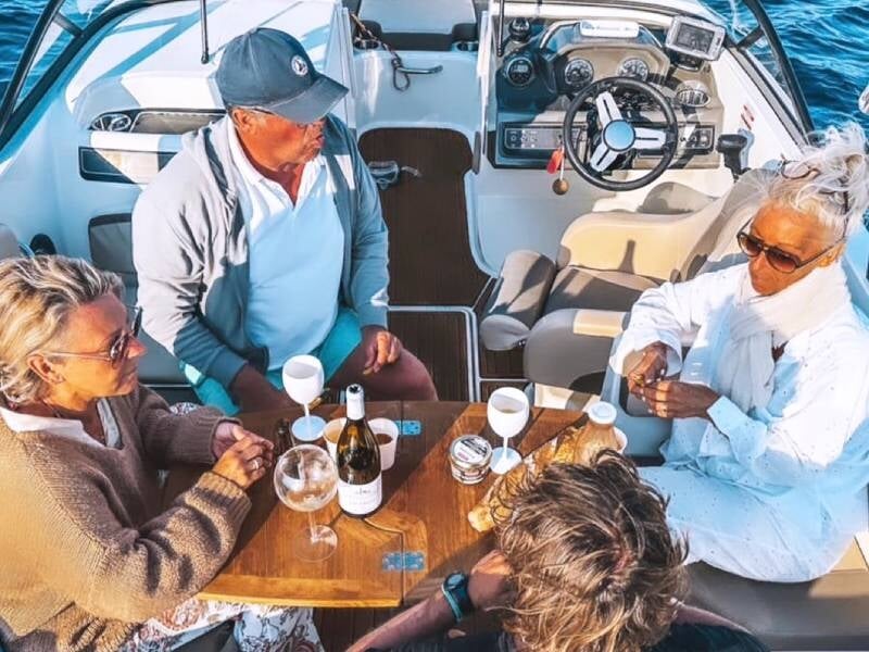 Quatre personnes discutent autour d'une table sur un bateau, avec des verres et une bouteille de vin lors d'une sortie en mer à Ramatuelle.