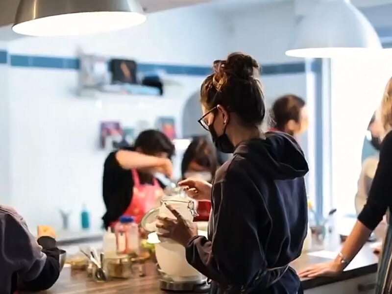 Personne en tablier et masque préparant un ingrédient dans un bol lors d'un cours de cuisine à Castelnau-le-Lez.