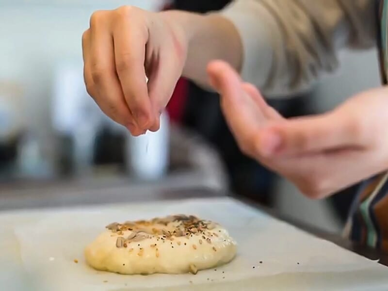 Gros plan sur une main saupoudrant des graines sur une pâte à pain avant la cuisson.