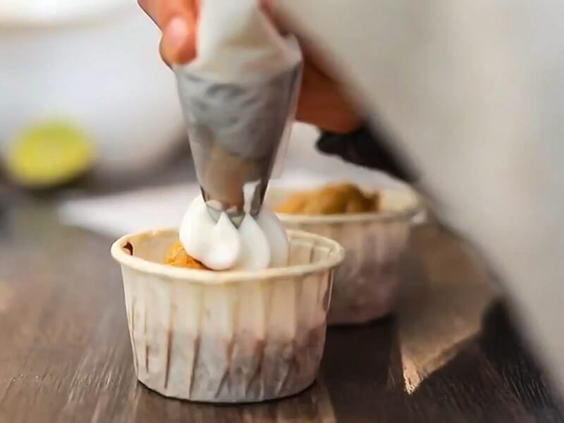 Main décorant un petit gâteau avec une poche à douille dans un cours de pâtisserie en groupe.
