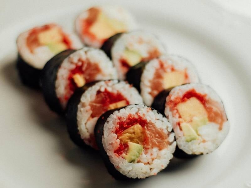 Plusieurs makis alignés sur une assiette blanche, garnis de riz, avocat, saumon et autres ingrédients frais, lors d'un atelier sushis à Marseille.