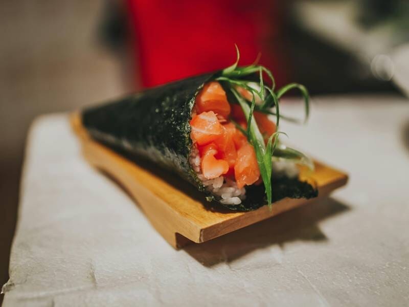 Temaki au saumon frais avec une garniture verte, présenté sur un support en bois sur une table.