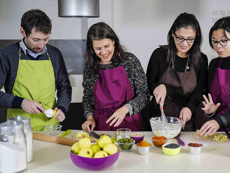 Quatre personnes en tabliers préparent ensemble des ingrédients frais dans une cuisine moderne et lumineuse.