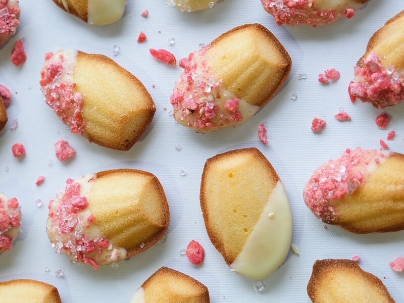Gros plan sur des madeleines décorées de chocolat blanc et de morceaux de fruits rouges croquants.