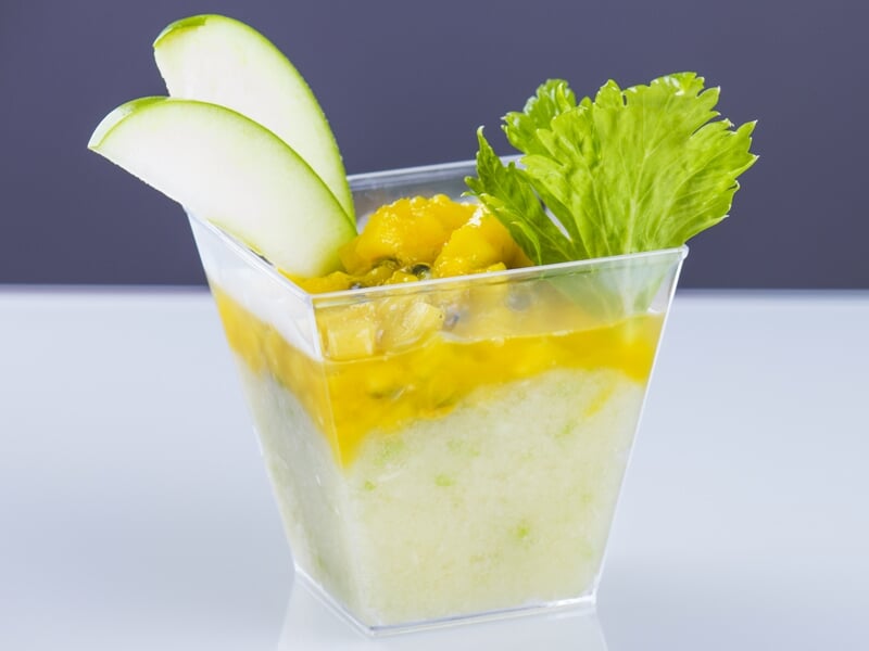 Verrine de dessert frais avec morceaux de pomme verte, purée de mangue et feuille de céleri en décoration.