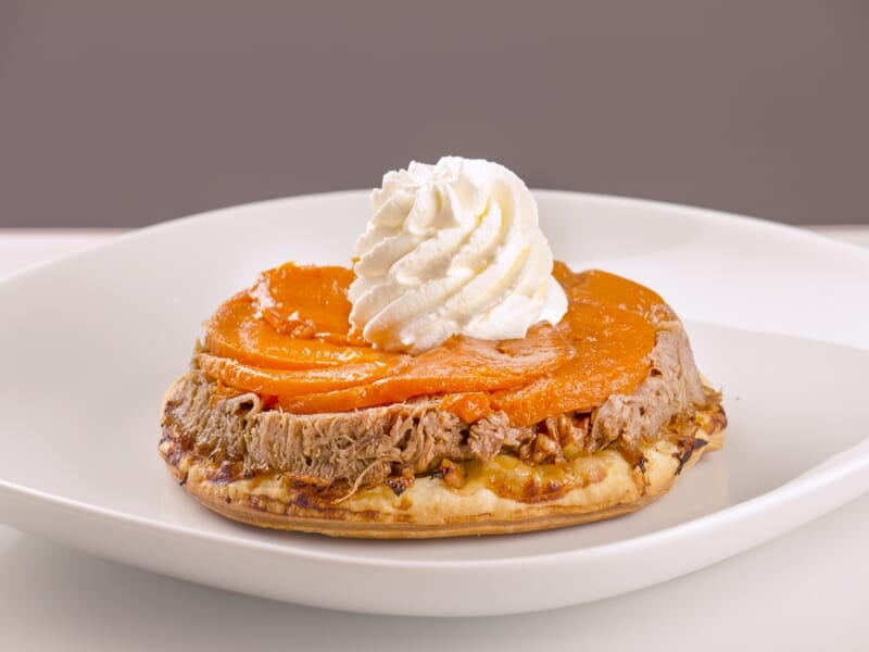 Tartelette garnie de purée de patate douce, crème fouettée et base croustillante sur assiette blanche.
