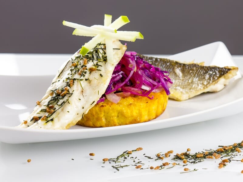 Plat gastronomique avec filet de poisson, purée colorée et salade de chou rouge sur assiette blanche.