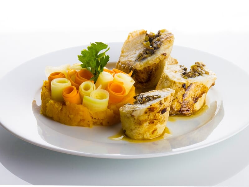 Roulades de viande farcie avec purée et décorations de légumes en spirale sur assiette blanche.