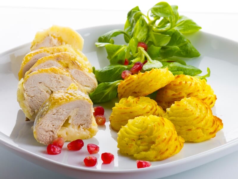 Tranches de volaille accompagnées de pommes duchesse et salade verte avec graines de grenade.