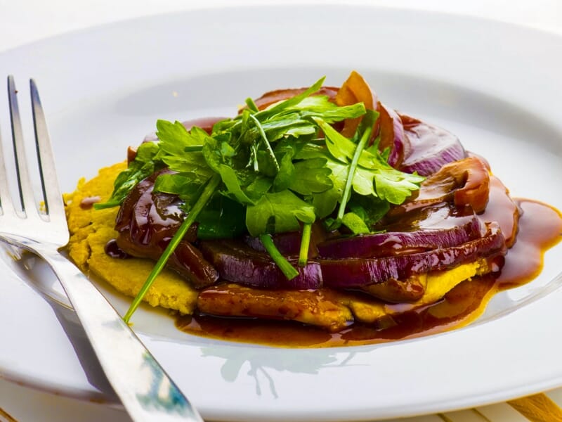 Plat végétarien avec légumes grillés, sauce brune et herbes fraîches sur assiette blanche.