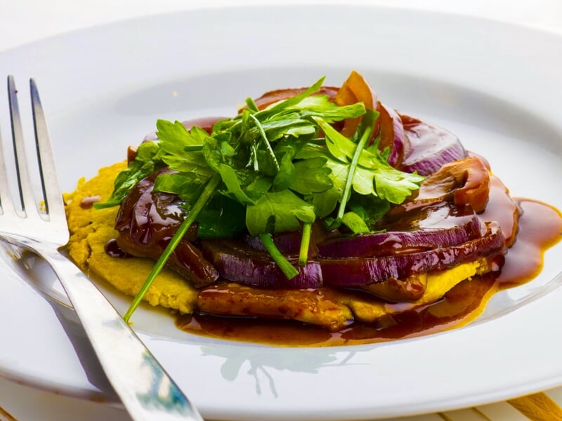 Plat végétarien avec légumes grillés, sauce brune et herbes fraîches sur assiette blanche.
