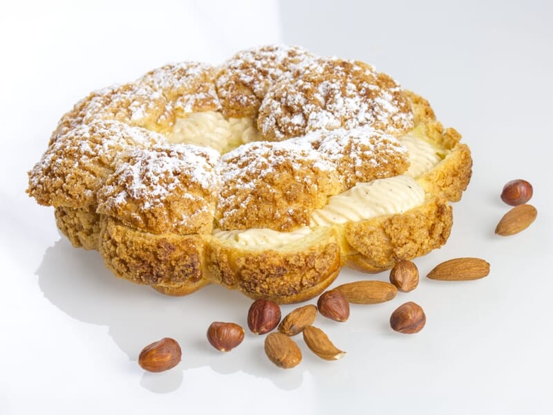 Gros plan sur une pâtisserie ronde garnie de crème, saupoudrée de sucre glace, avec des noisettes autour.
