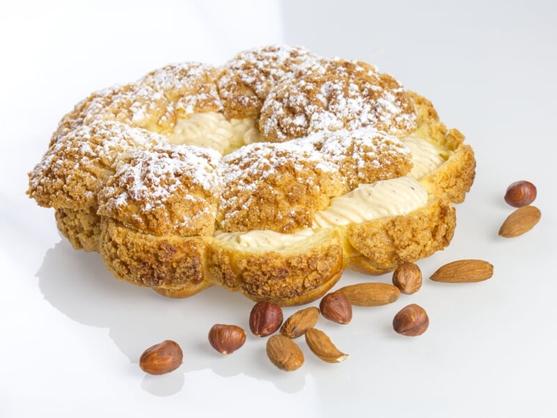 Gros plan sur une pâtisserie ronde garnie de crème, saupoudrée de sucre glace, avec des noisettes autour.
