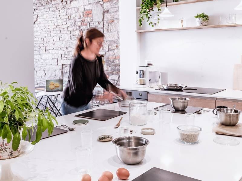Personne en mouvement dans une cuisine moderne avec ingrédients et ustensiles sur un plan de travail blanc.